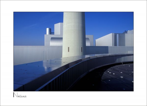 Schornstein eines Heizkraftwerks mit Himmel und Edelstahlfassaden