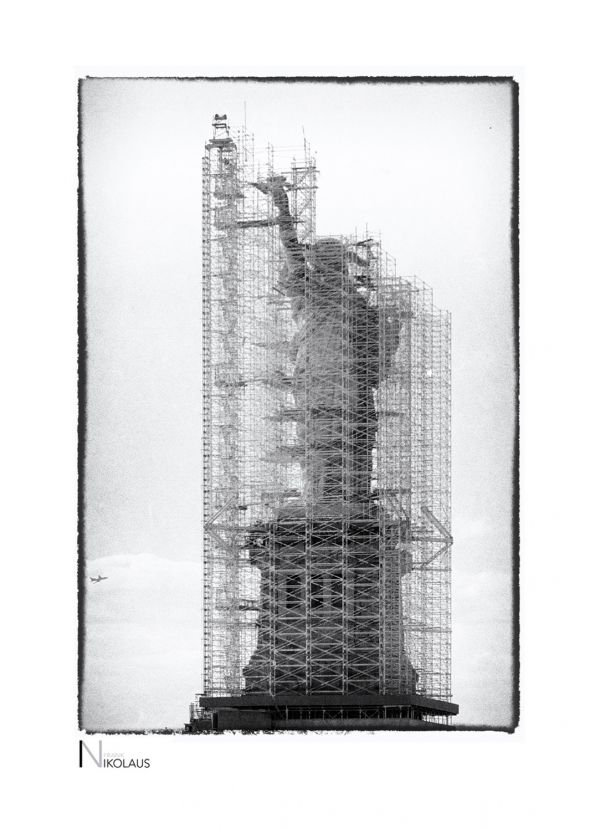 Eingerüstete Freiheitsstatue mit Flugzeug im Hintergrund in New York